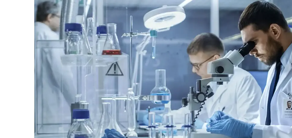 A busy lab, with two scientists, with the one in the foreground looking into a microscope