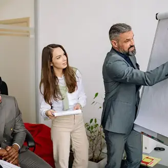 Three office workers are actively engaged writing on a whiteboard paper easel