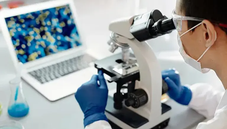 Over the shoulder view of a scientist looking down a microscope