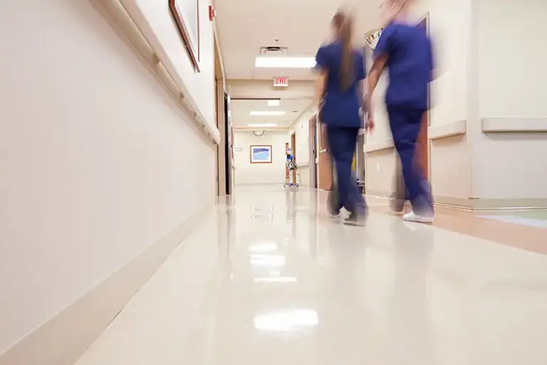 Two nurses, seen from behind, as they walk down a hospital corridor