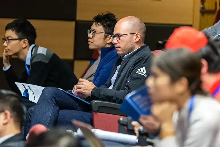 View of a group of professional delegates sat in a lecture theatre, focus on the unseen presenter 