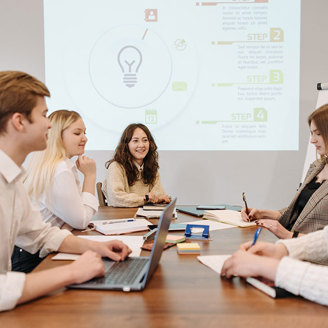 Team of office workers sit at a large table with the presentation projected on the rear wall