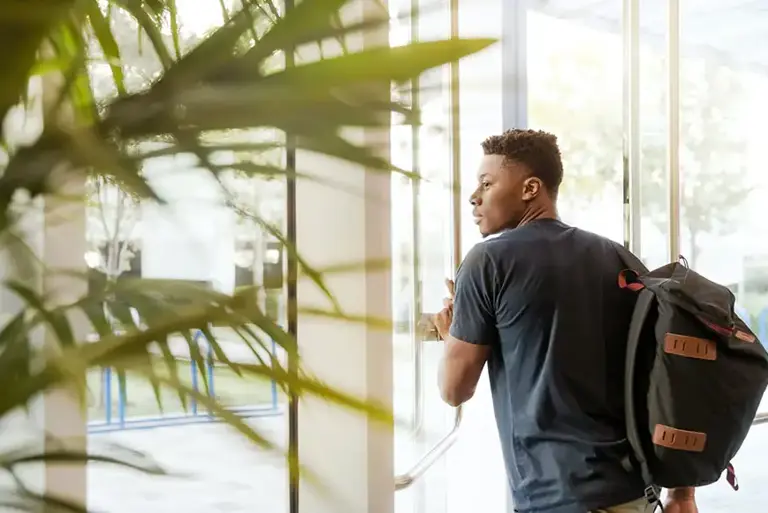 Young man with backpack, walks through a large glass revolving door at an office building  