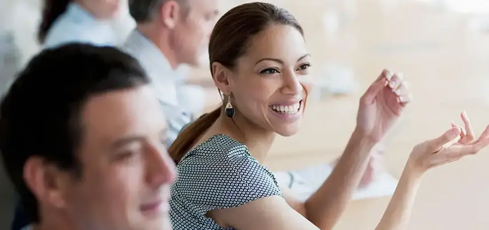 Woman at a meeting, sits smiling at the unseen delegates